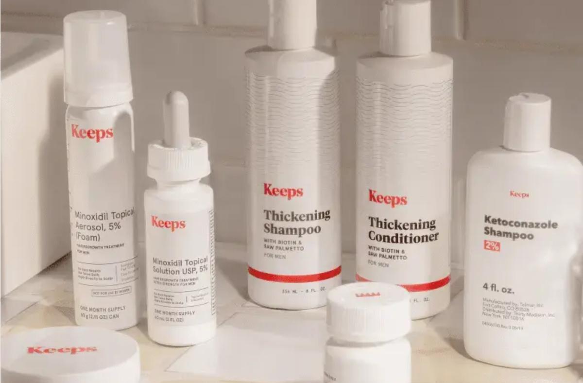 Several bottles of white Keeps hair thickening and hair regrowth products in a white tiled bathroom.